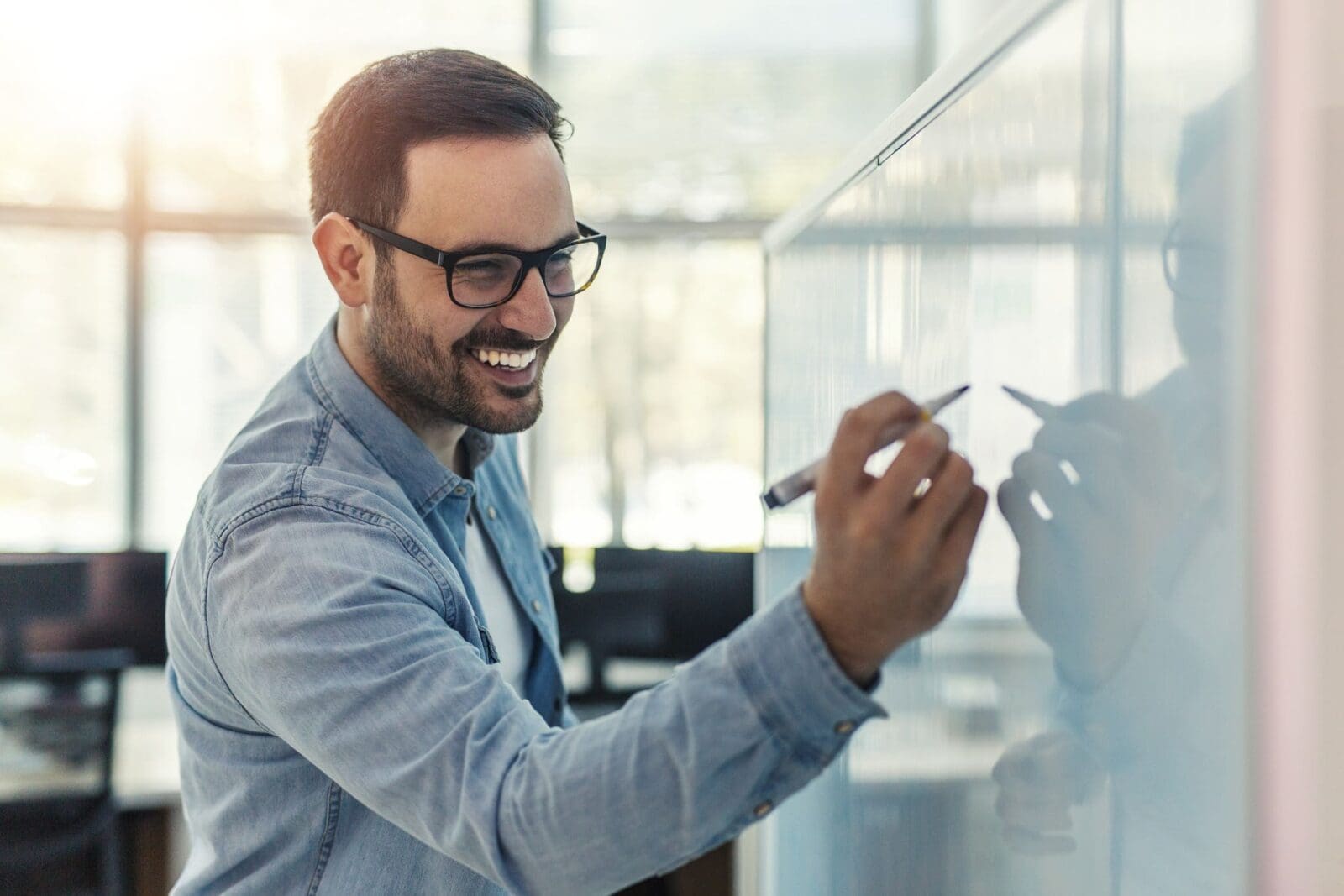 A smiling businessman writing a strategic goal on a whiteboard. Credit: https://www.istockphoto.com/portfolio/JelenaDanilovic?mediatype=photography