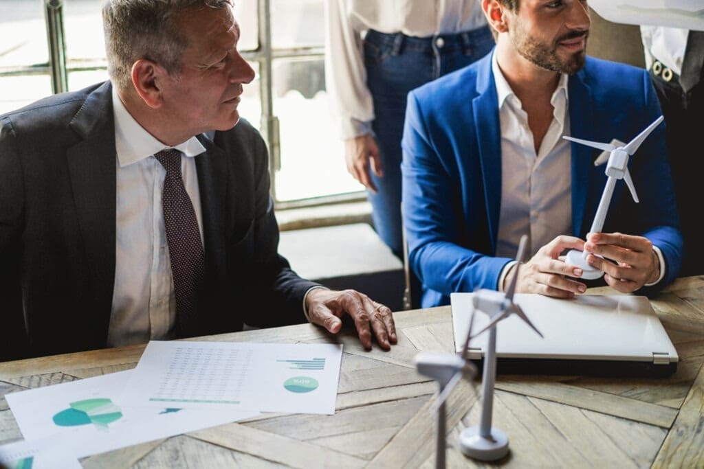 Two men discussing a report about ESG performance, one holding a wind turbine. Credit: https://www.istockphoto.com/portfolio/DisobeyArt?mediatype=photography