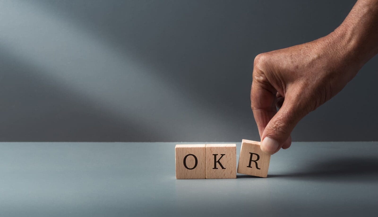 A hand placing wooden blocks on a table with the letters OKR. Credit: https://www.istockphoto.com/portfolio/robatthepub?mediatype=photography
