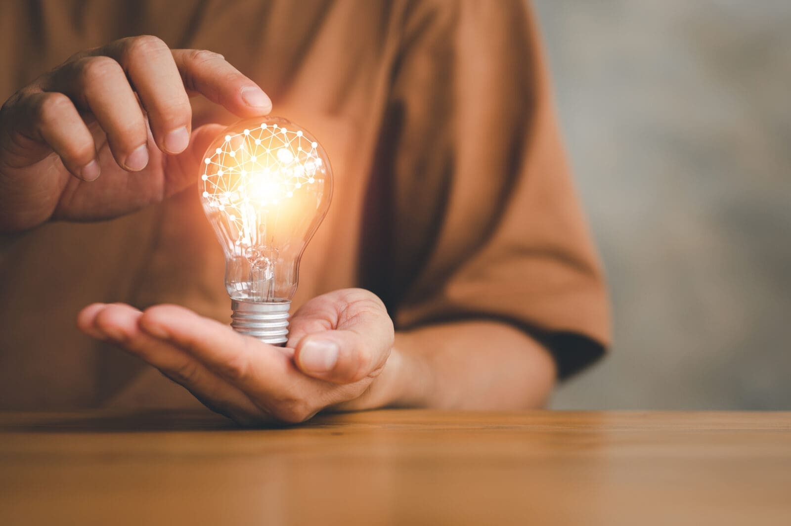 A male's hands holding a glowing lightbulb, containing digital connections shaped like a brain. CREDIT: https://www.istockphoto.com/portfolio/Anawat_s