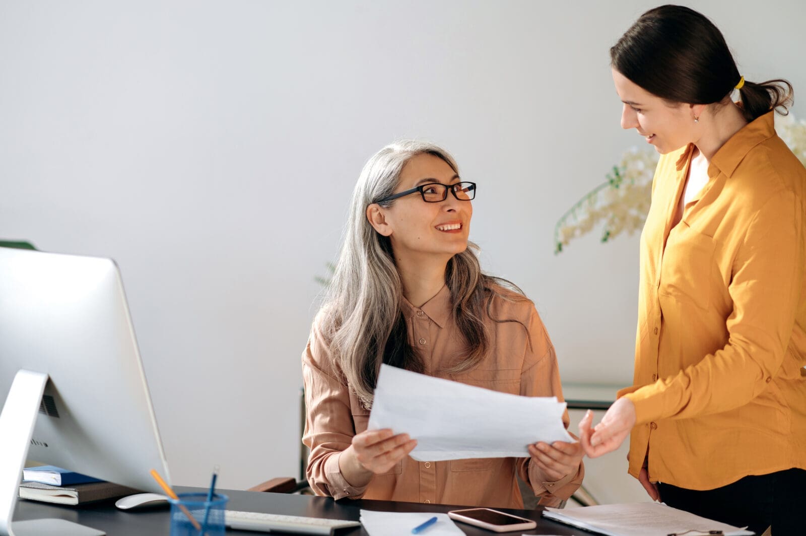 Mature Asian woman happily discusses a KPI chart with a colleague. CREDIT: https://www.istockphoto.com/portfolio/KaterynaOnyshchuk