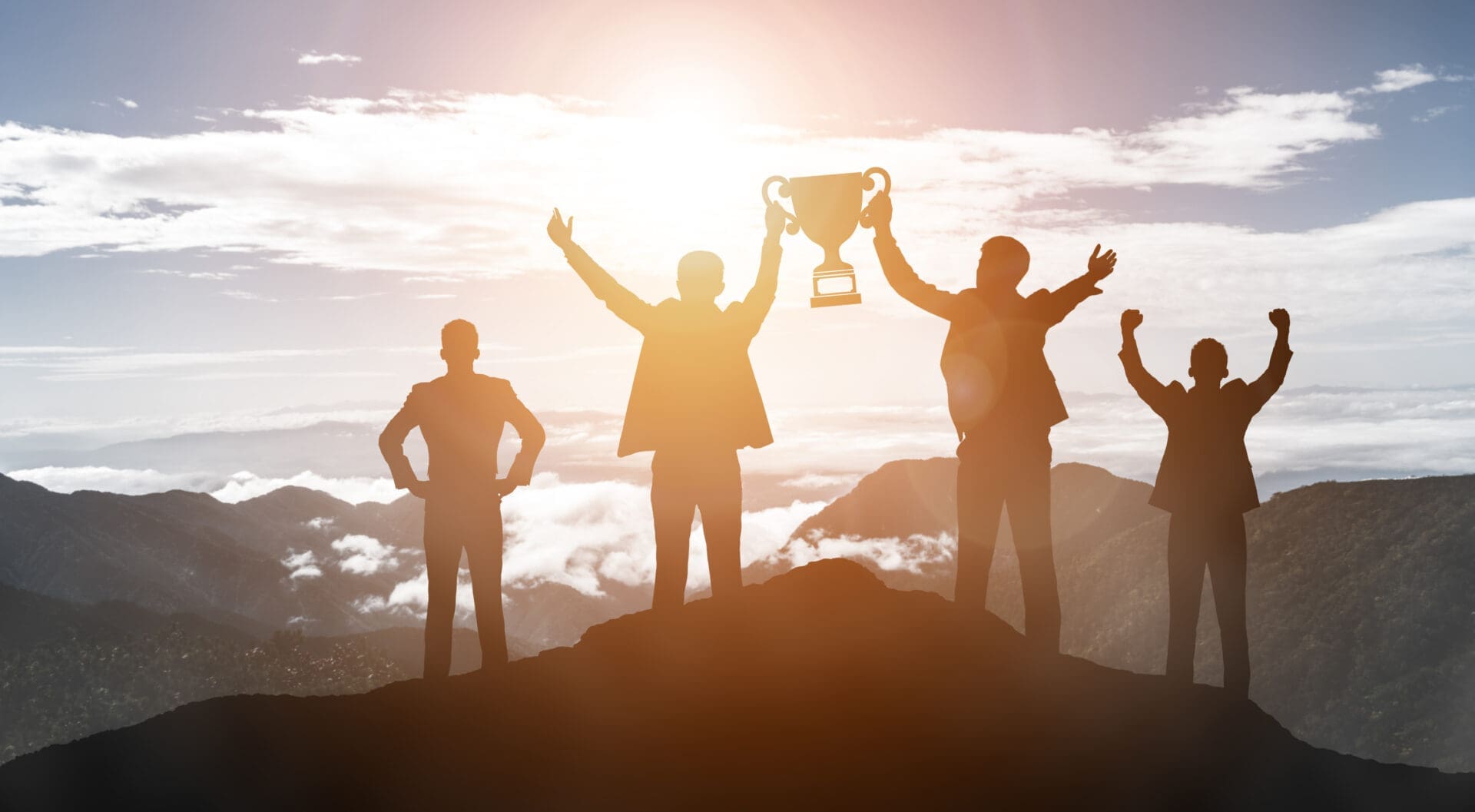 A team standing on the mountain top with a trophy for achieving the best. CREDIT: https://www.istockphoto.com/portfolio/BluePlanetStudio