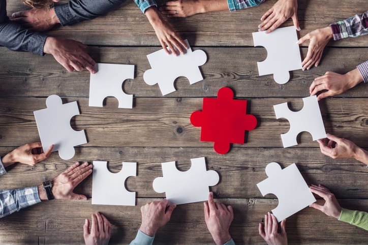 Business team assembling jigsaw puzzle pieces around a central piece.